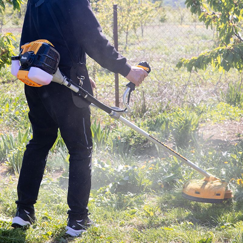 Робота бензиновим тримером біля паркану