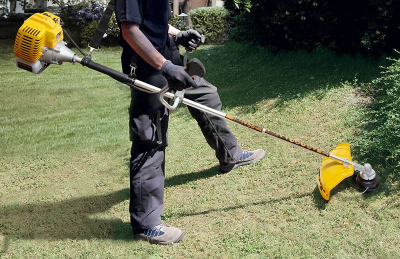 Чоловік косить траву бензиновим тримером