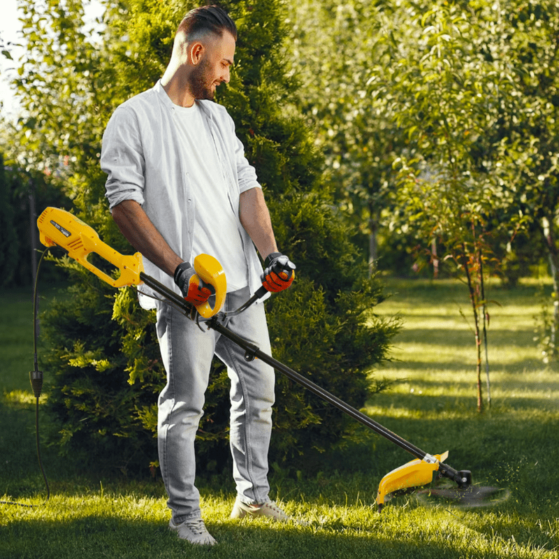 Чоловік стриже траву електричним тримером у саду