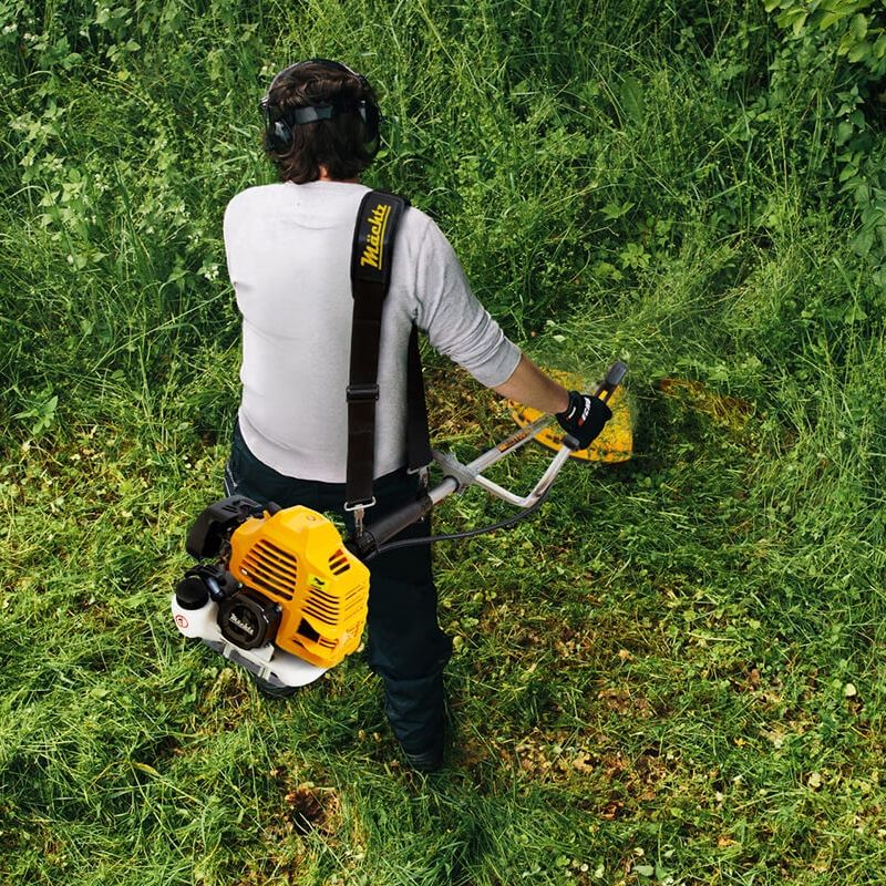 Чоловік із бензокосою розчищає густу траву