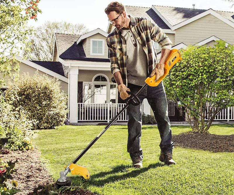 Мужчина подстригает газон триммером