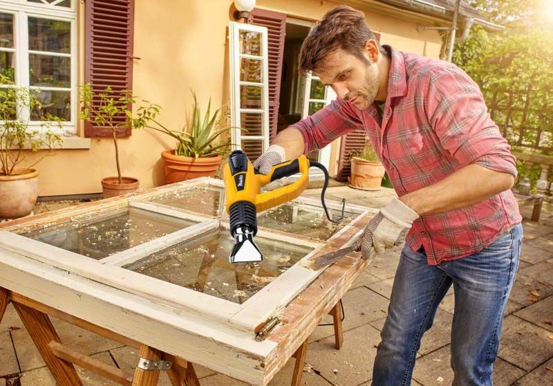 Чоловік працює будівельним феном з рамою вікна