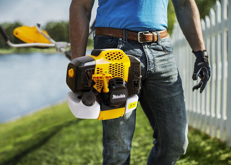 Чоловік із бензиновим тримером біля паркану