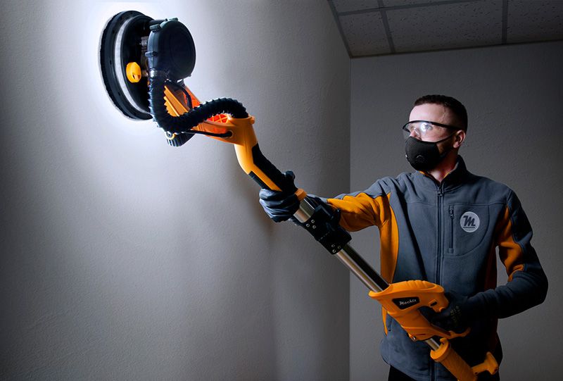 Майстер шліфує стіну шліфмашиною