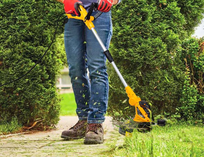 Людина працює електротримером у саду